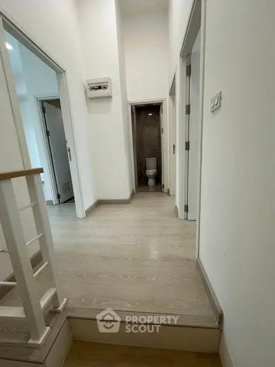 Bright hallway with wooden flooring leading to a modern bathroom in a stylish home.