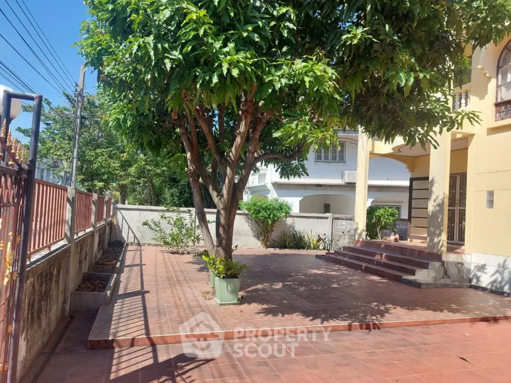 Charming residential entrance with spacious tiled patio and lush greenery, perfect for outdoor relaxation.