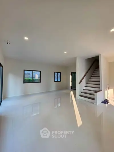 Spacious modern living room with staircase and large windows, perfect for natural light.
