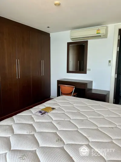 Cozy bedroom with large bed, built-in wooden wardrobe, and modern air conditioning unit, perfect for comfortable urban living.