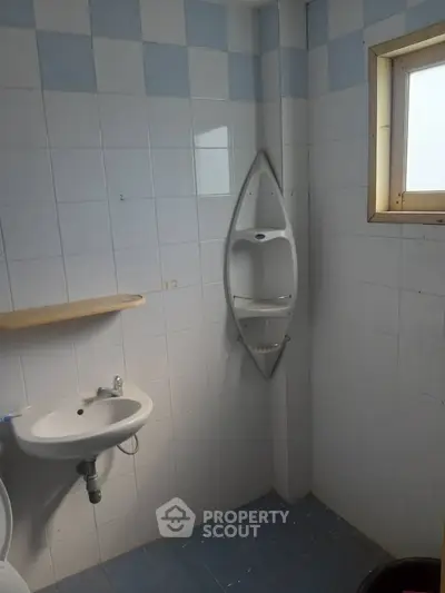 Compact bathroom with wall-mounted sink and corner shower shelf, featuring blue and white tiled walls.