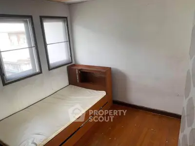 Cozy minimalist bedroom with wooden flooring and natural light from two windows.