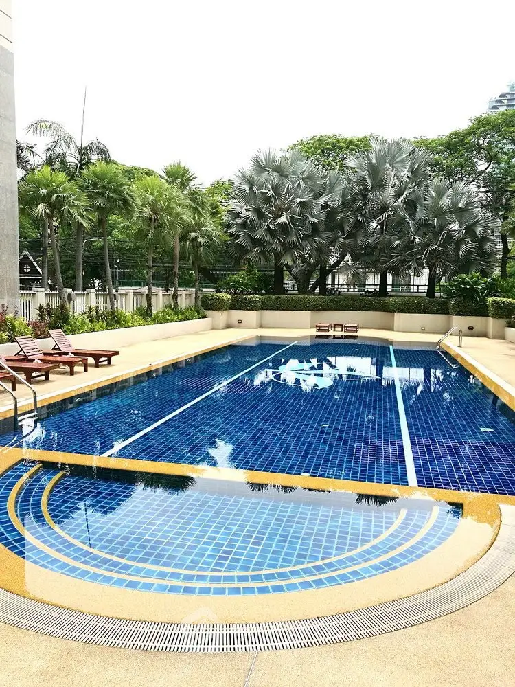 Luxurious outdoor swimming pool with lush greenery and sun loungers in a serene setting.