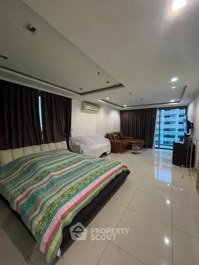 Spacious bedroom with modern decor and city view, featuring a cozy seating area.