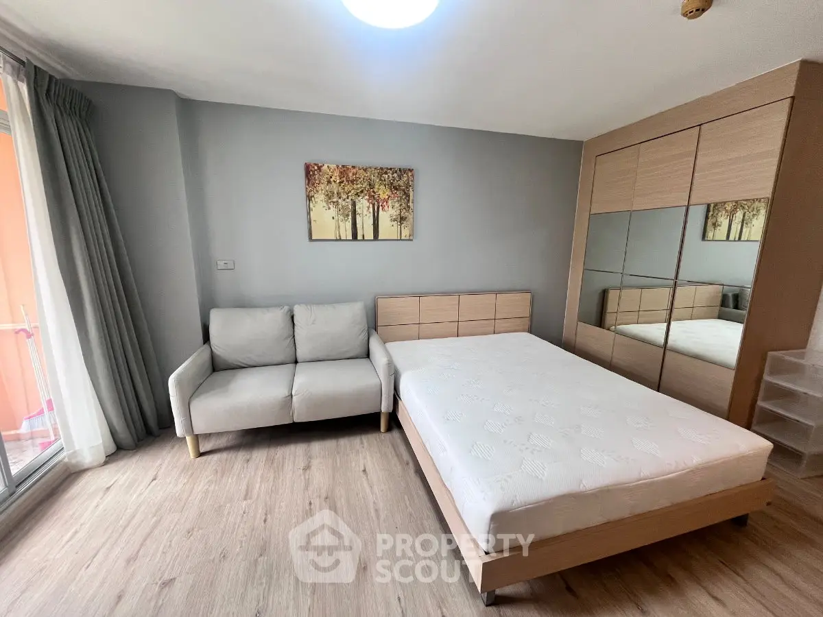 Modern bedroom with cozy sofa, mirrored wardrobe, and large window for natural light.