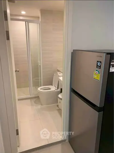 Modern bathroom with glass shower and adjacent stainless steel refrigerator in compact space.