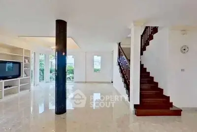 Spacious living room with modern staircase and large windows offering natural light.