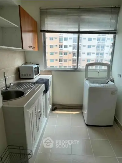 Compact kitchen with washing machine and microwave, featuring a large window with city view.