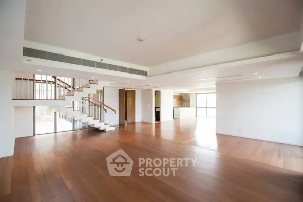Spacious open-plan living room with wooden flooring and modern staircase in luxury apartment.