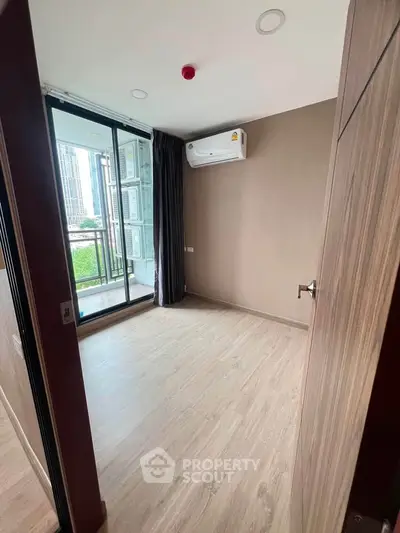 Spacious bedroom with balcony access and modern air conditioning unit in urban apartment.