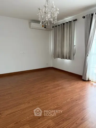 Spacious empty room with elegant chandelier and wooden flooring, perfect for customization.