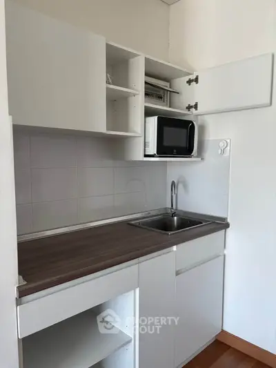 Compact modern kitchen with sleek cabinetry and microwave, ideal for small spaces.
