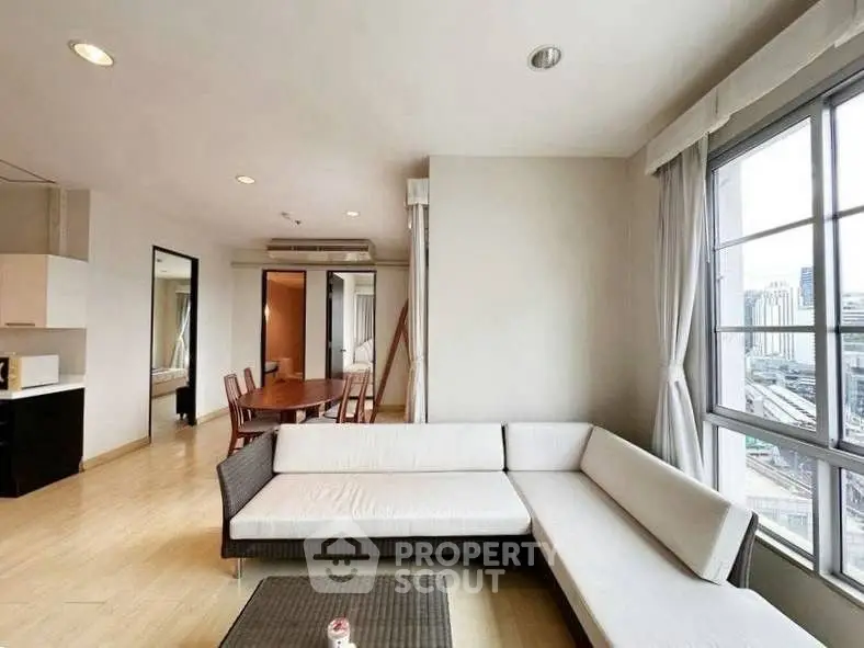 Spacious modern living room with large windows and city view, featuring a stylish corner sofa and dining area.