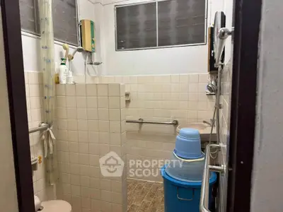 Compact bathroom with tiled walls and safety handrails, featuring a shower and essential amenities.