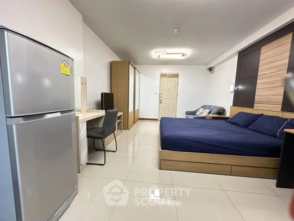 Modern studio apartment with sleek design, featuring a cozy bed, workspace, and stainless steel fridge.