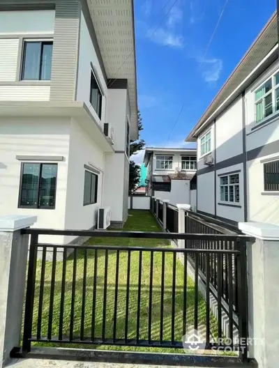 Modern residential building exterior with green lawn and black metal gate under clear blue sky.