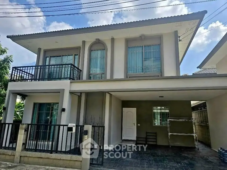 Modern two-story house with balcony and carport in a suburban neighborhood.