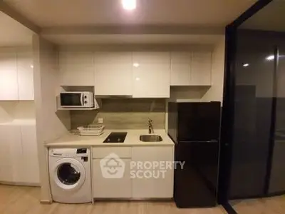 Modern kitchen with sleek cabinets, washing machine, and black fridge in a compact layout.