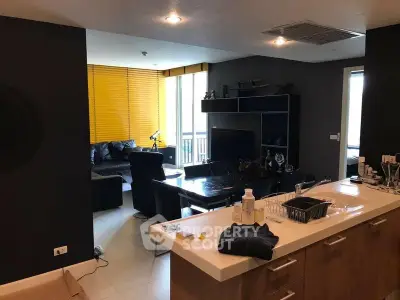 Modern living room with open kitchen, stylish black furniture, and large windows for natural light.