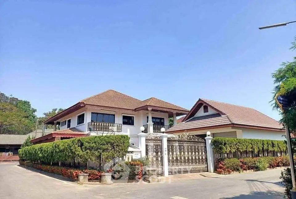 Charming two-story house with lush greenery and gated entrance under clear blue sky.
