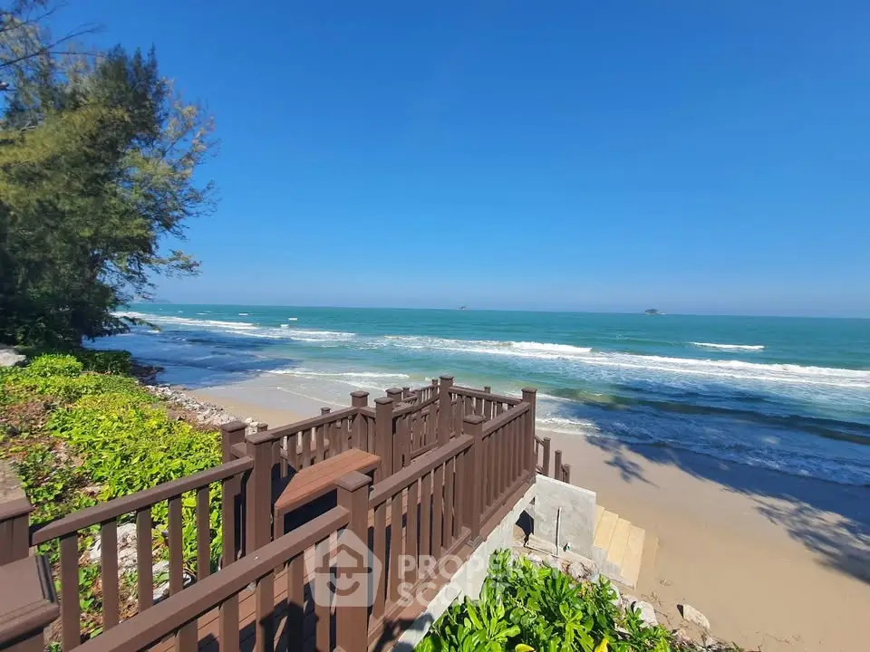 Stunning beachfront view with wooden railing and lush greenery under clear blue sky.