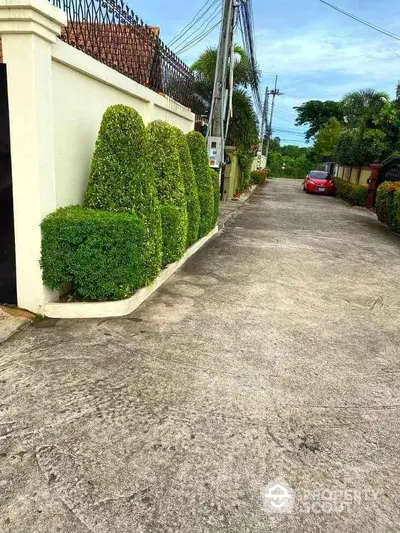 Charming residential street with manicured hedges and parked red car, ideal for tranquil living.