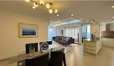 Spacious modern living room with open kitchen and elegant dining area, featuring stylish lighting and large windows.