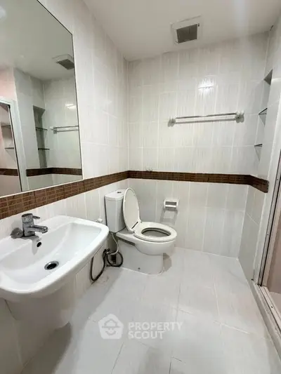 Modern bathroom with sleek white fixtures and tiled walls, featuring a spacious shower area.