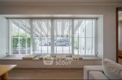 Spacious living room with large window and cozy seating area, offering a serene view of the outdoors.