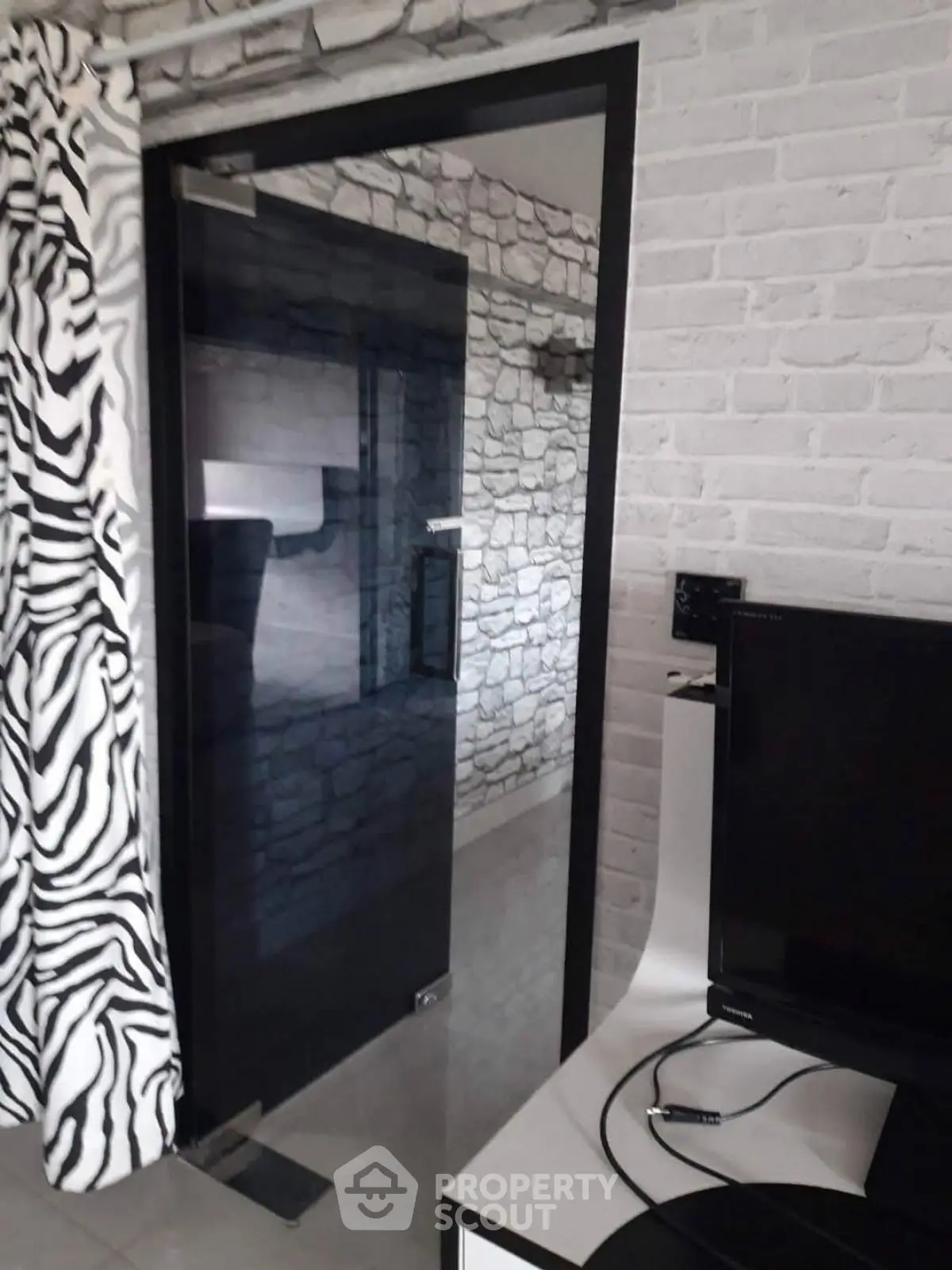 Modern interior with glass door and zebra-patterned curtain, featuring a sleek TV setup.
