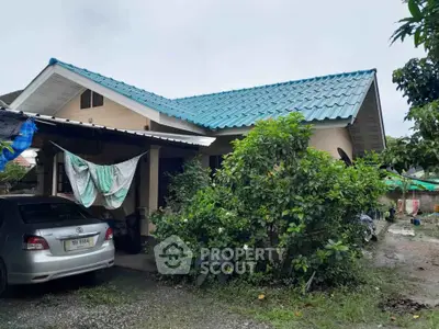 Charming single-story house with blue roof and lush greenery in a serene neighborhood.