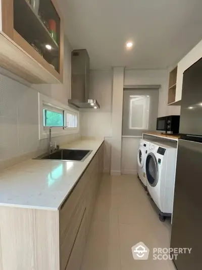 Modern kitchen with sleek cabinetry and built-in appliances, featuring a washing machine and dryer.