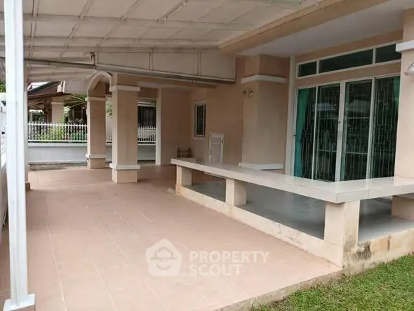 Spacious covered patio area with tiled flooring and garden view, perfect for outdoor relaxation.