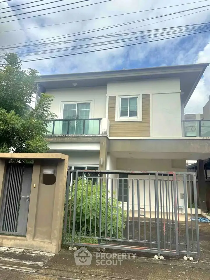 Modern two-story house with gated entrance and lush greenery, perfect for family living.