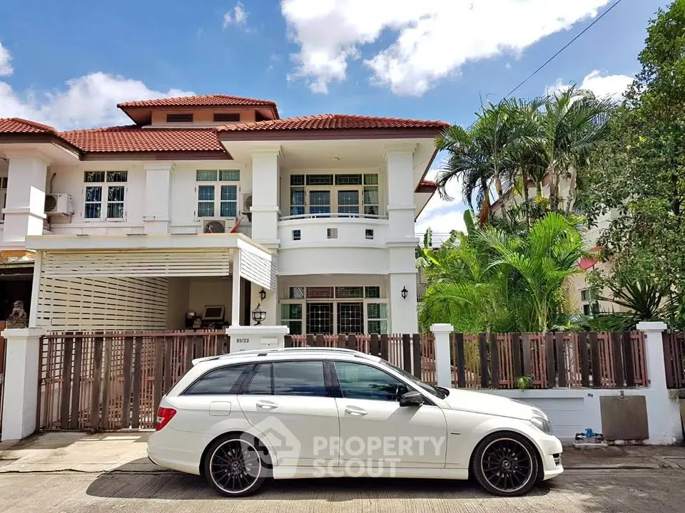 Charming two-story house with red-tiled roof and lush greenery, featuring a white car parked in front.