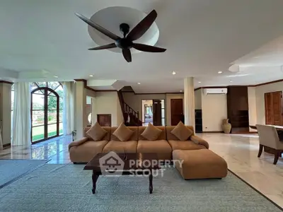 Spacious living room with elegant sofa and ceiling fan, featuring large windows and open layout.