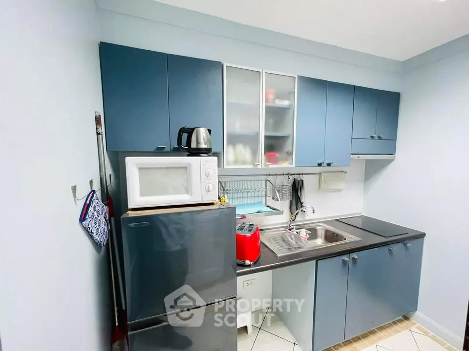 Compact kitchen with modern blue cabinets and appliances, including microwave and fridge, ideal for efficient cooking.