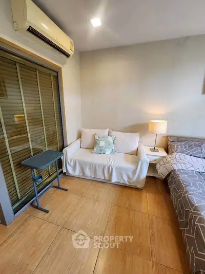 Cozy bedroom with sofa and modern decor, featuring air conditioning and wooden flooring.