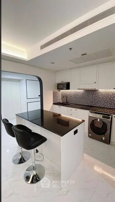 Modern kitchen with sleek black countertops and stylish bar stools in a contemporary apartment.