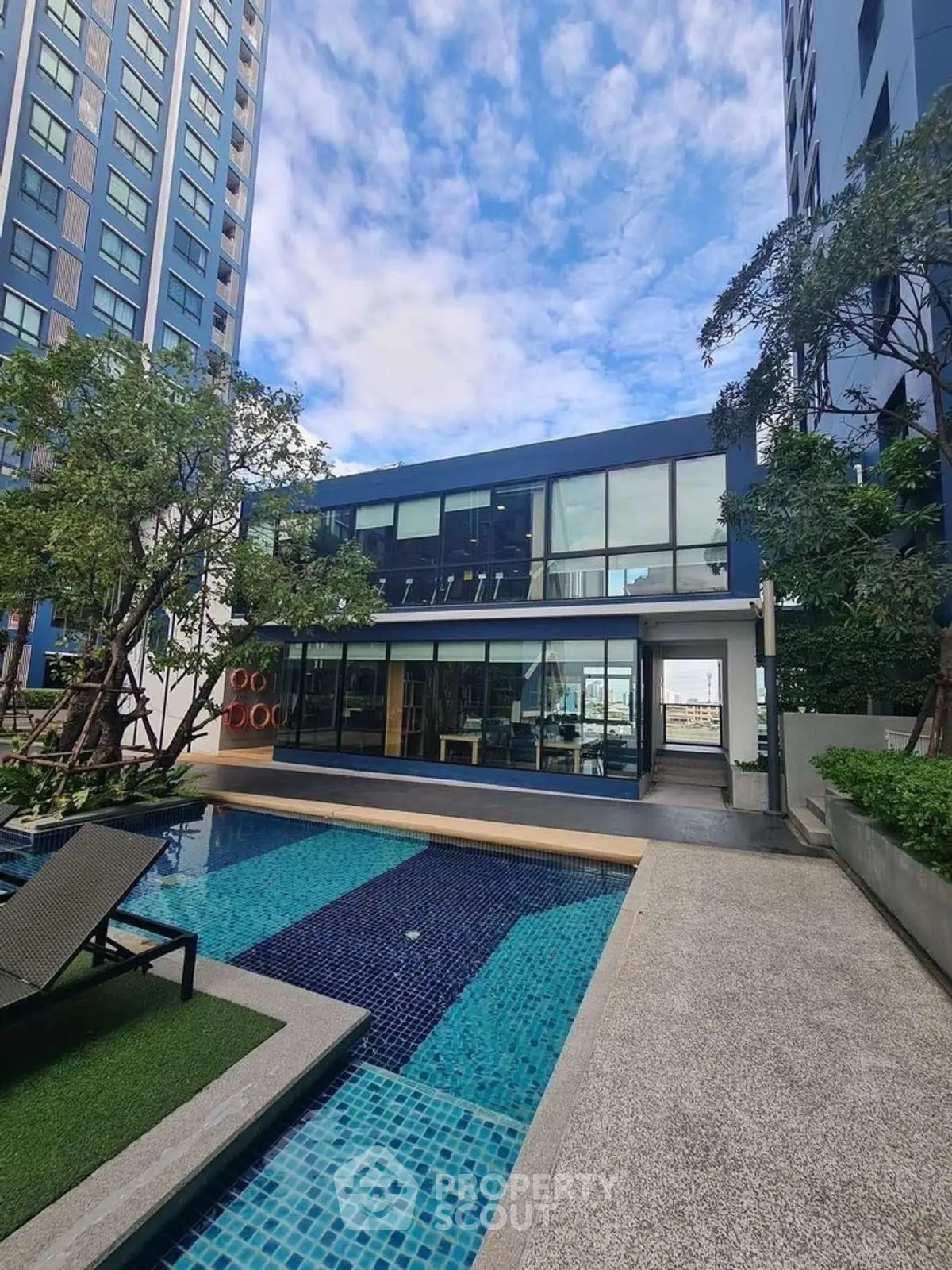 Modern apartment complex with pool and lush greenery under a clear blue sky.
