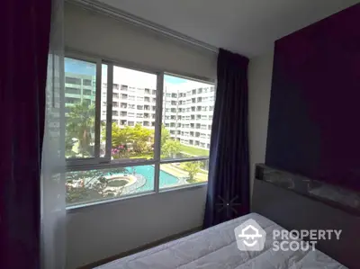 Cozy bedroom with large window offering pool and garden view in modern apartment complex.