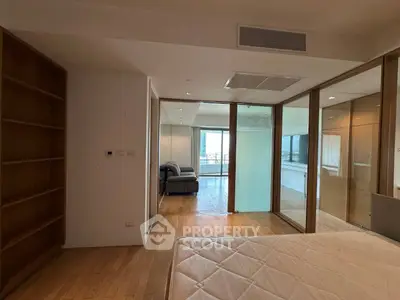 Spacious modern bedroom with wooden flooring and glass partitions leading to a cozy living area.