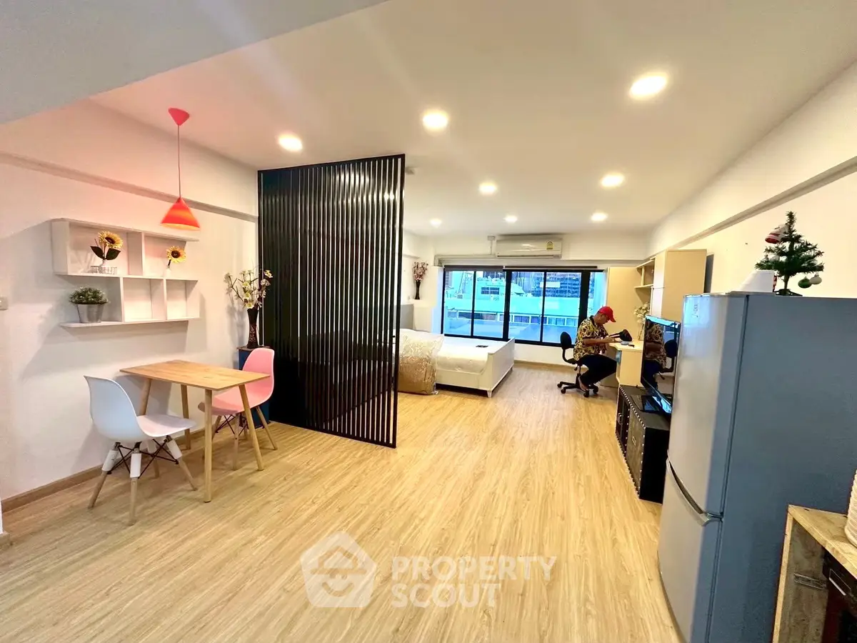 Modern open-plan living space with dining area, workspace, and balcony access, featuring stylish decor and ample lighting.