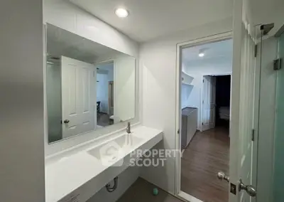 Modern bathroom with sleek sink and mirror, leading to a cozy bedroom with wooden flooring.