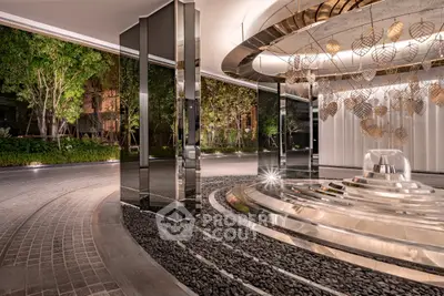 Luxurious building entrance with modern design and elegant lighting, featuring a stunning circular fountain and lush greenery.