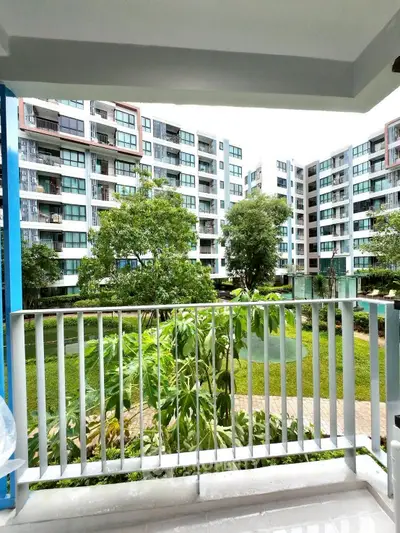Spacious balcony with a view of lush garden and modern apartment complex.