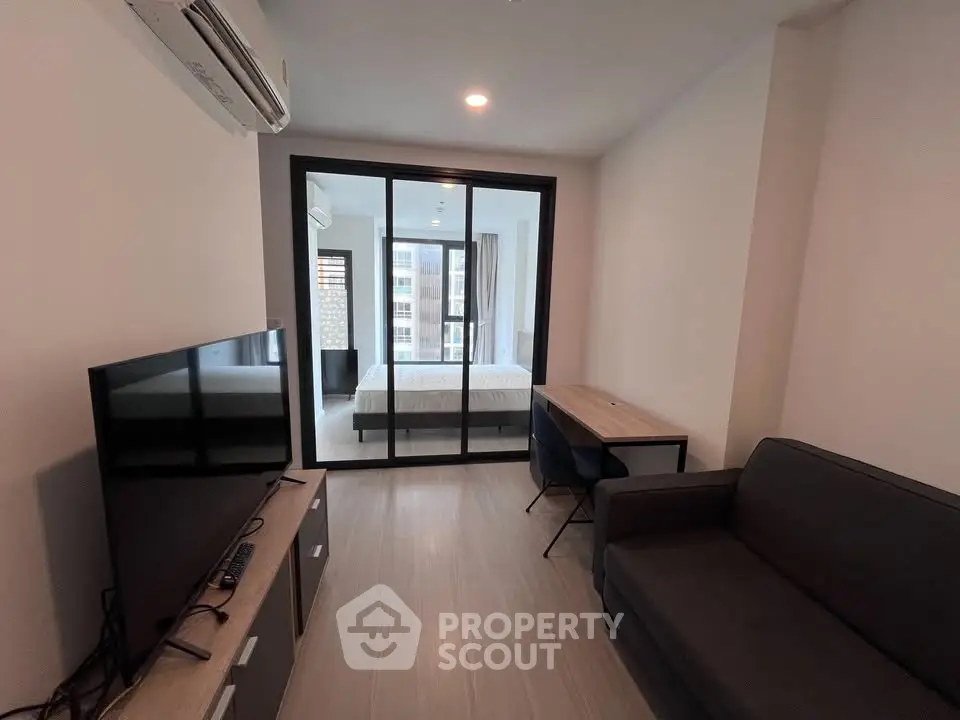 Modern apartment interior with living room and bedroom separated by glass doors, featuring sleek furniture and neutral tones.