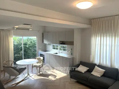 Modern living room with open kitchen, natural light, and stylish furniture.