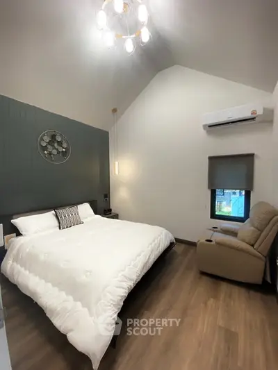 Modern bedroom with high ceiling, cozy recliner, and stylish decor in a contemporary home.