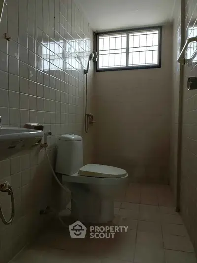 Compact bathroom with tiled walls and window, featuring a toilet and sink.